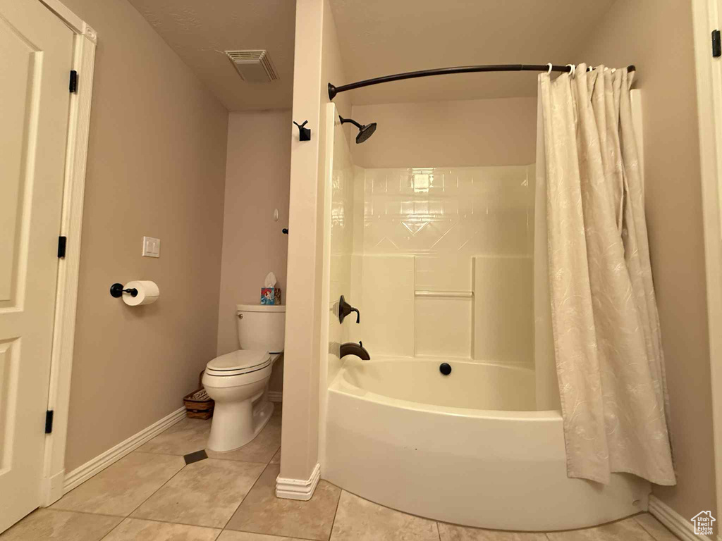 Bathroom with toilet, shower / bath combo, tile patterned flooring, and baseboards