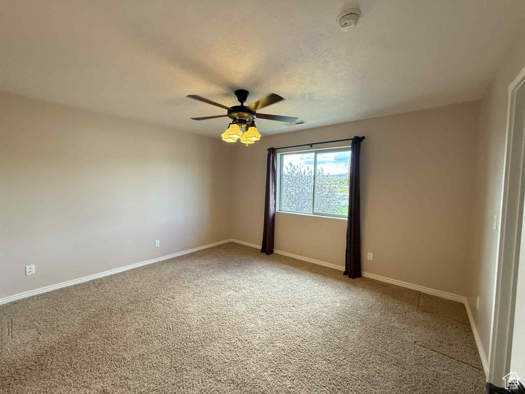 Carpeted spare room with a ceiling fan, baseboards, a smoke detector, and a textured ceiling