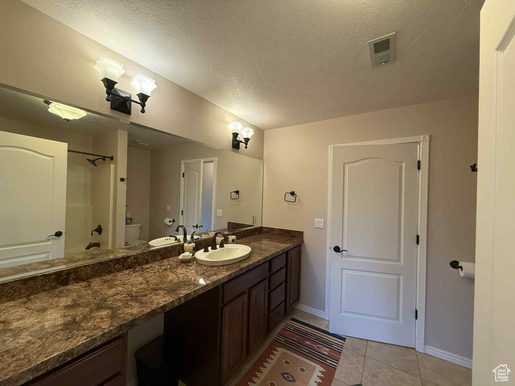 Bathroom featuring vanity, toilet, tile patterned flooring, baseboards, and a textured ceiling