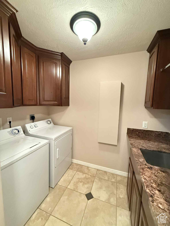 Washroom featuring independent washer and dryer, cabinet space, baseboards, a textured ceiling, and light tile patterned floors