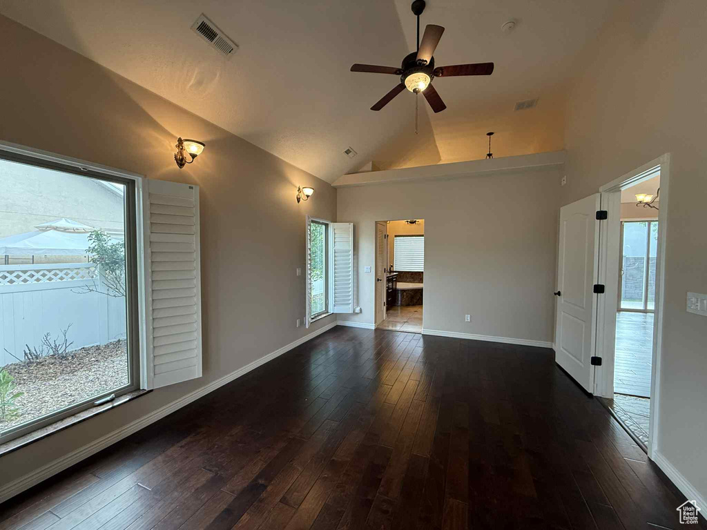Unfurnished living room with healthy amount of natural light, dark wood-style flooring, a ceiling fan, and high vaulted ceiling