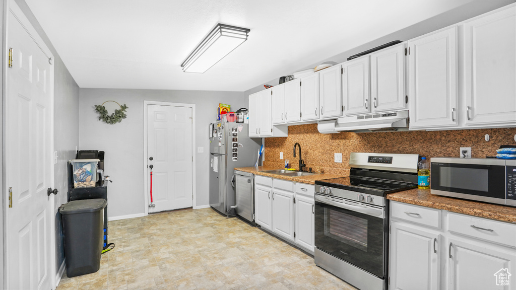 Kitchen with stainless steel appliances, a sink, under cabinet range hood, and white cabinetry
