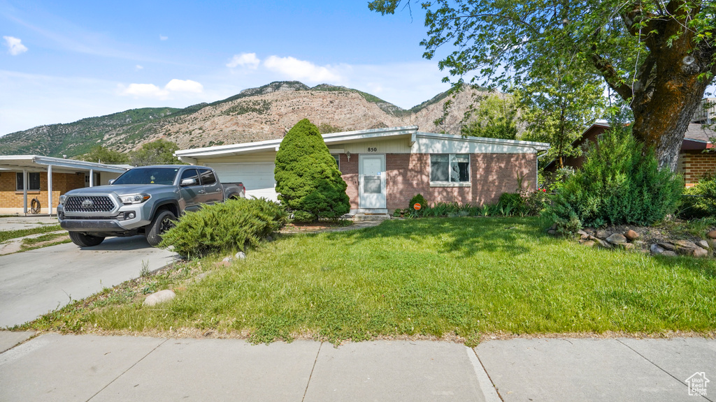 View of front of house featuring a mountain view, an attached garage, a front lawn, and concrete driveway
