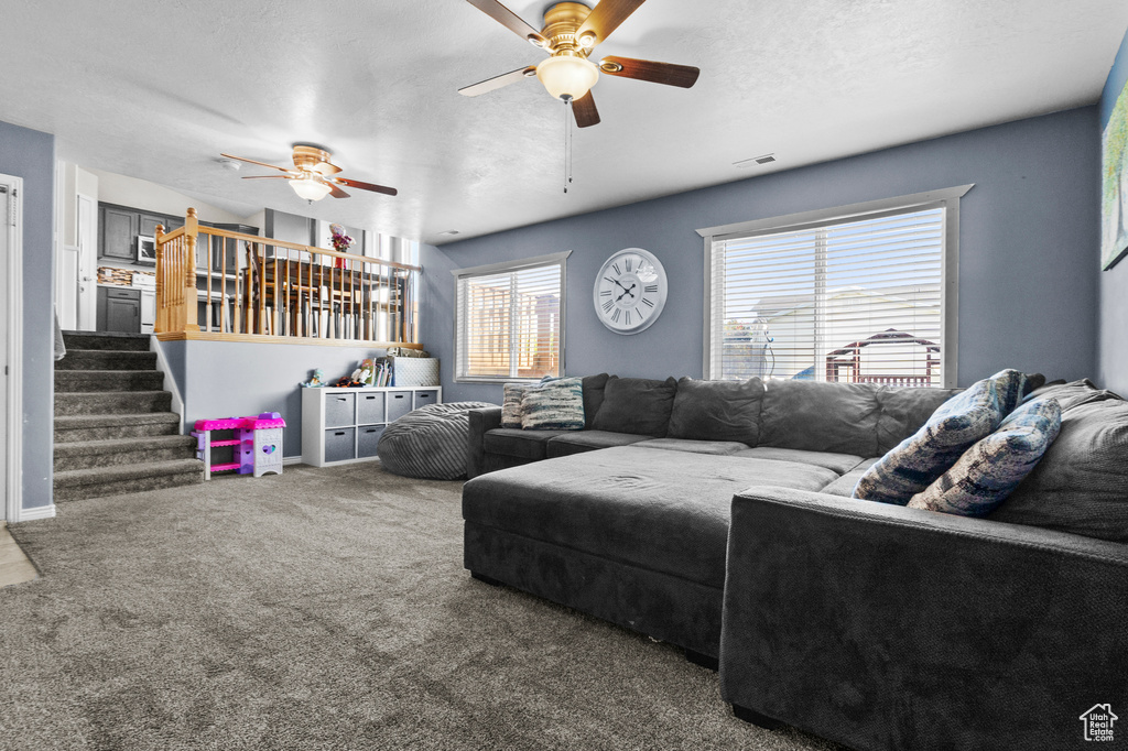 Carpeted living room with ceiling fan and stairs
