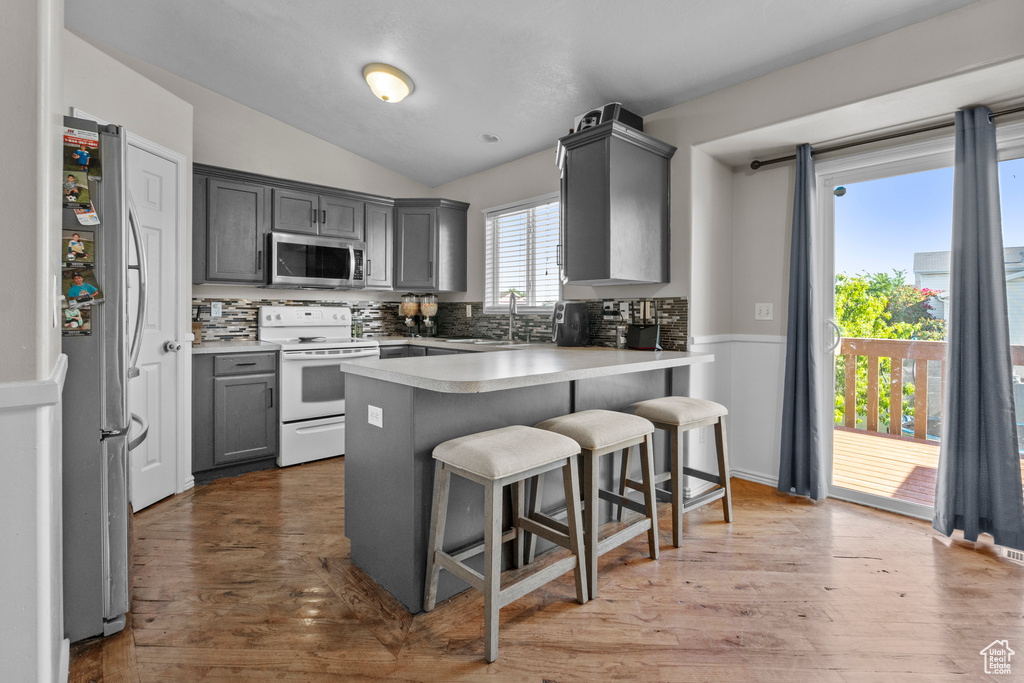 Kitchen with appliances with stainless steel finishes, gray cabinets, lofted ceiling, tasteful backsplash, and a sink