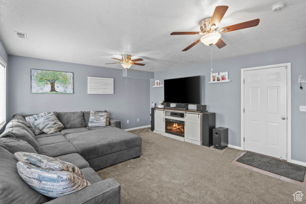 Living room featuring ceiling fan, a glass covered fireplace, carpet, and baseboards