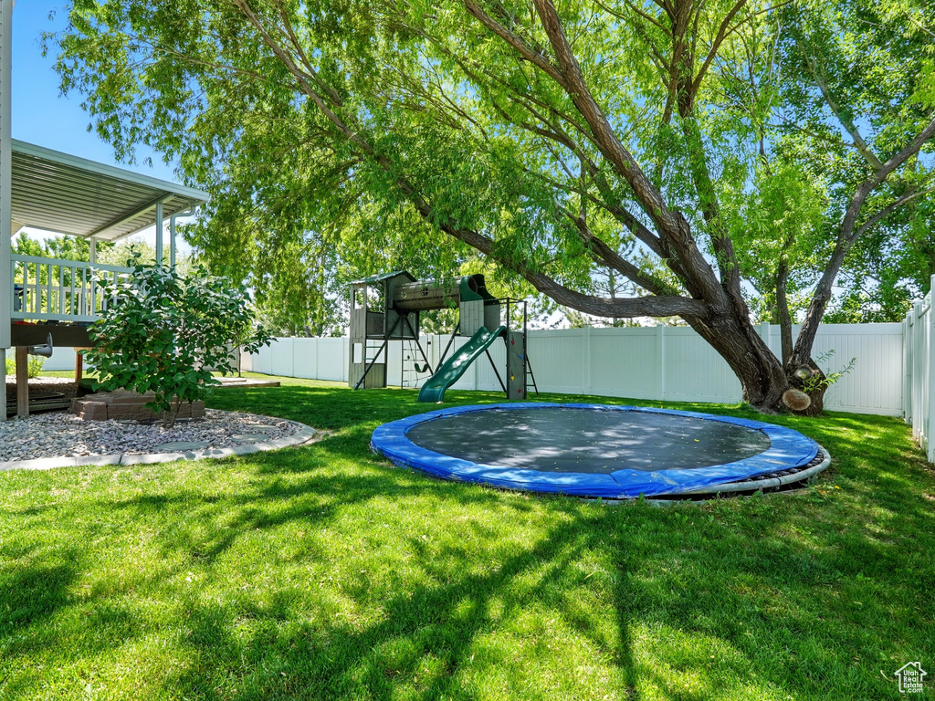View of yard featuring a trampoline, a playground, and a wooden deck