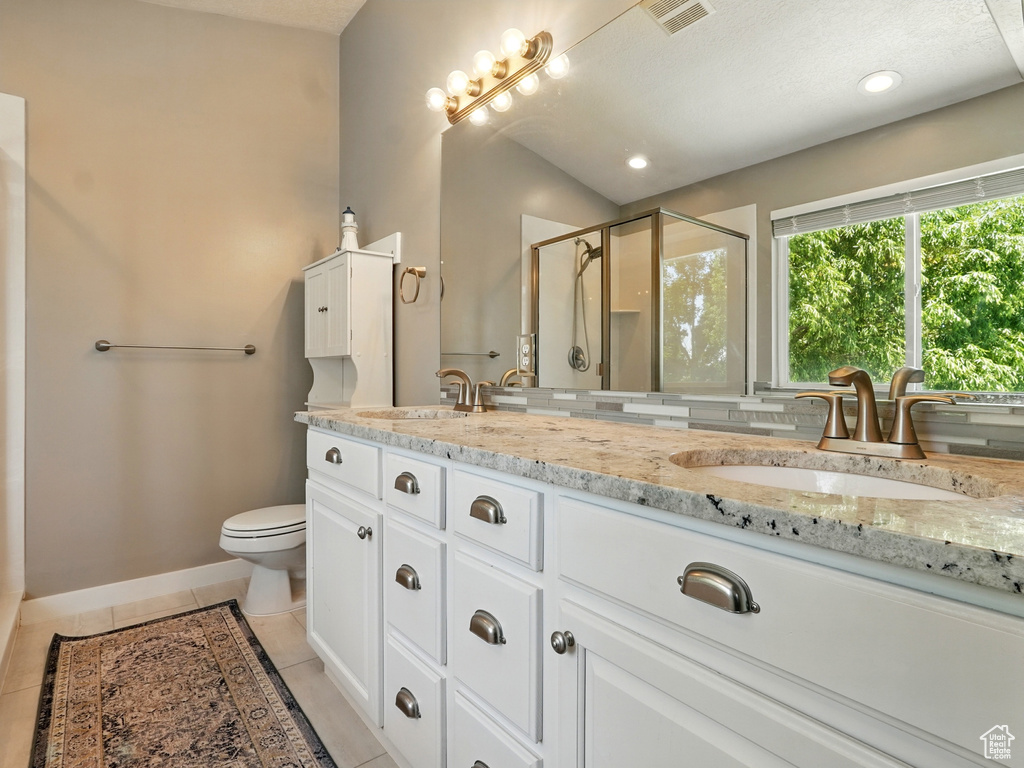 Bathroom featuring a shower stall, double vanity, toilet, tile patterned floors, and baseboards