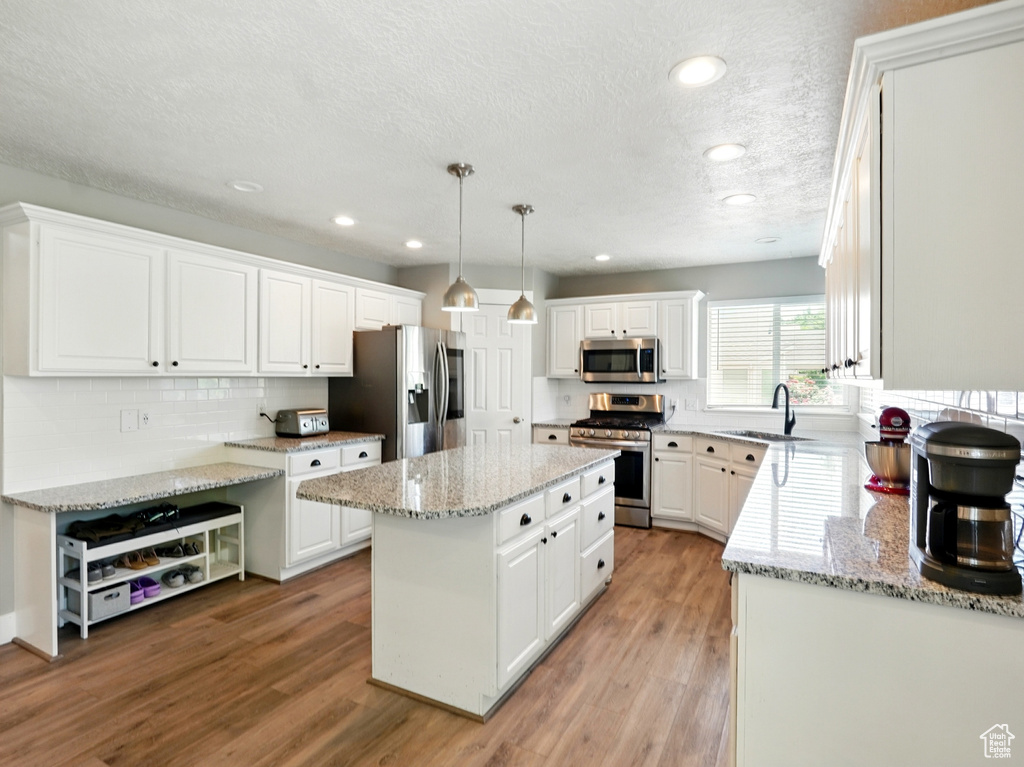 Kitchen featuring stainless steel appliances, a sink, a center island, a textured ceiling, and white cabinets