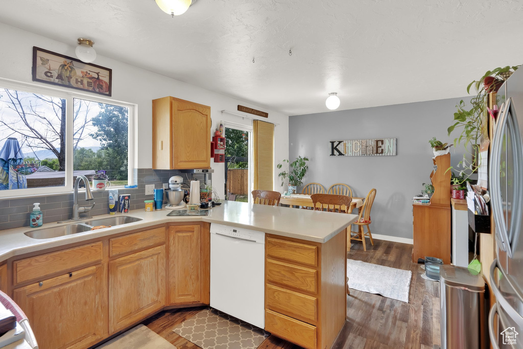 Kitchen with dishwasher, a peninsula, dark wood finished floors, decorative backsplash, and light countertops