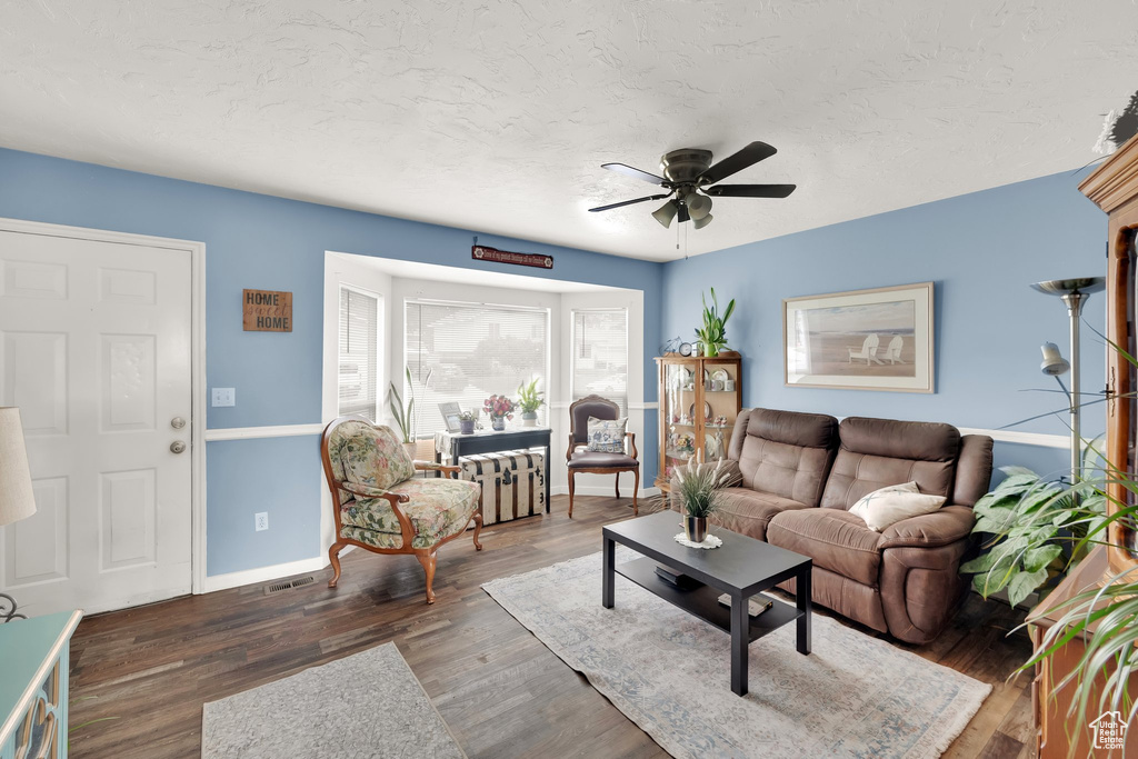 Living area featuring ceiling fan, wood finished floors, baseboards, and a textured ceiling