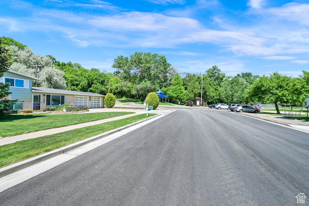 View of asphalt street featuring sidewalks, curbs, and view of scattered trees