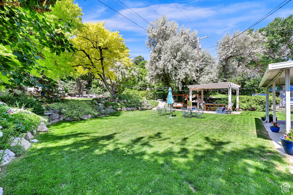 View of green lawn featuring a pergola, a patio, and view of scattered trees