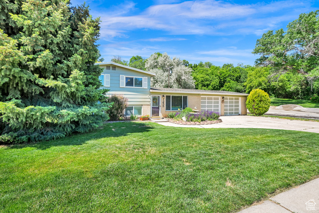 Split level home with concrete driveway, brick siding, a front yard, and a garage