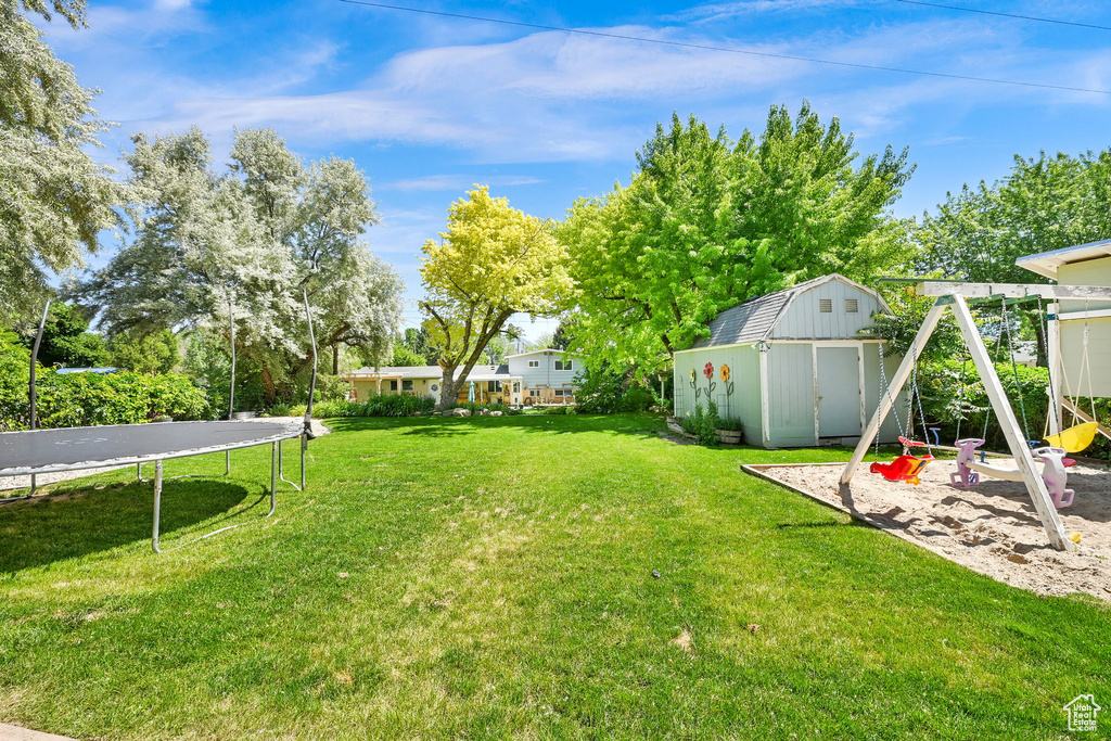 View of green lawn featuring a trampoline and a playground
