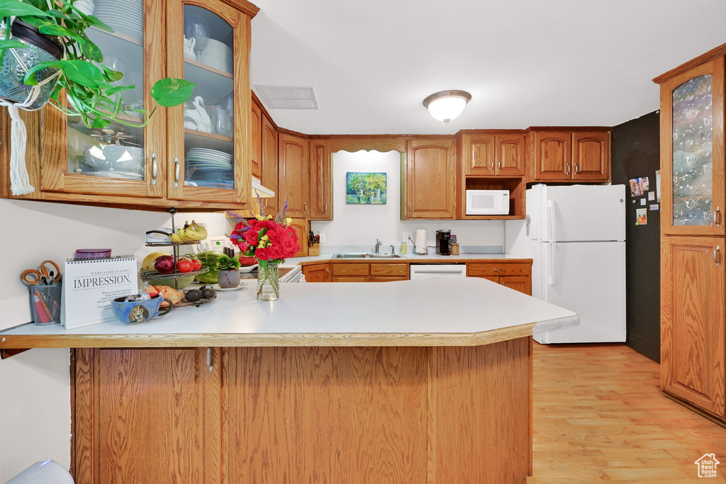 Kitchen featuring white appliances, a sink, a peninsula, light countertops, and light wood-style floors
