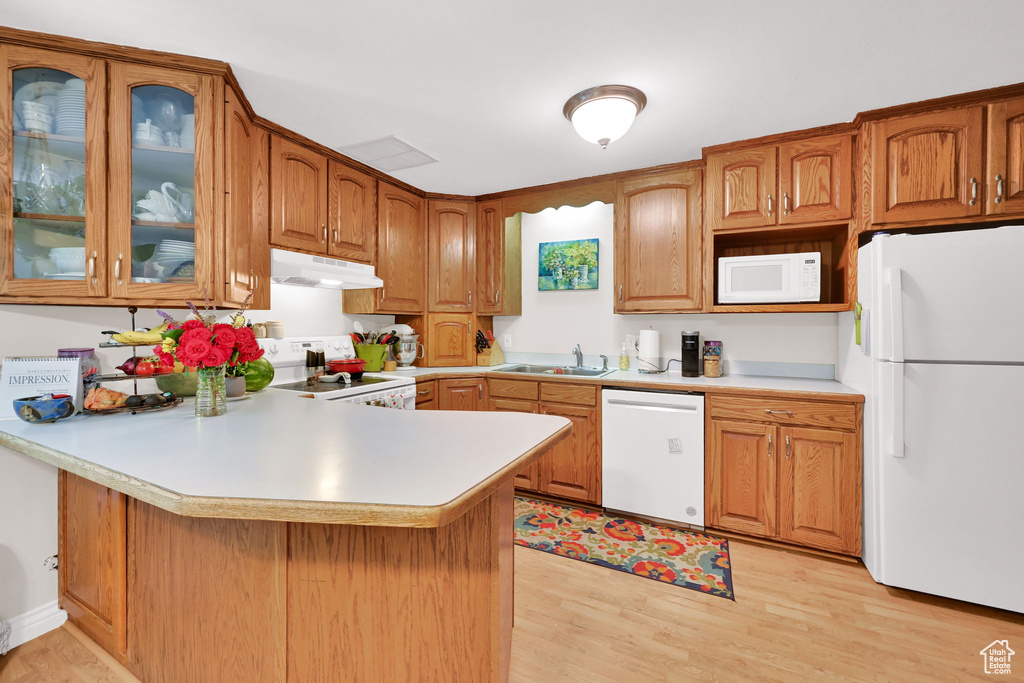 Kitchen with white appliances, a peninsula, under cabinet range hood, and light countertops