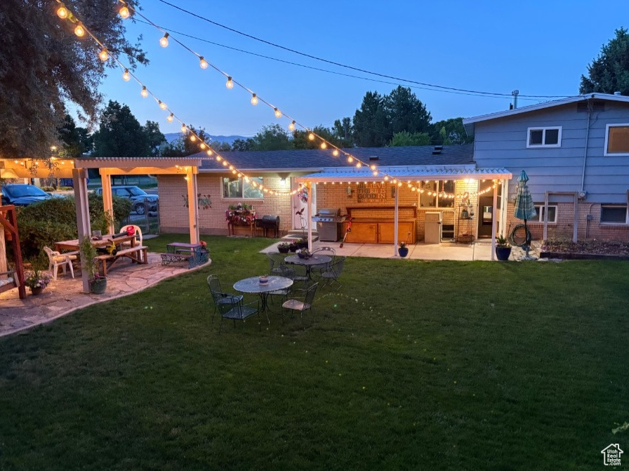 Back of house featuring a patio area, a pergola, a covered hot tub, and a lawn