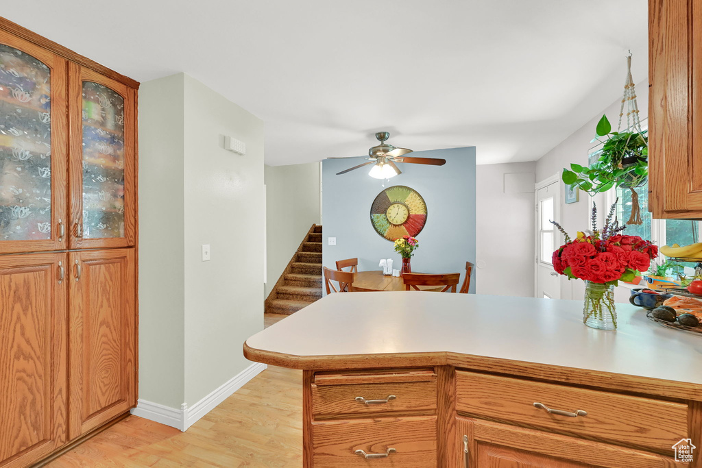 Kitchen featuring light wood-style flooring, a peninsula, a ceiling fan, glass insert cabinets, and light countertops