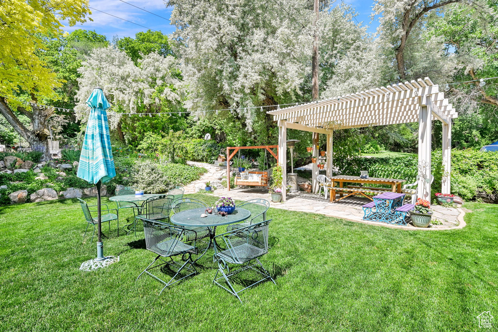 View of green lawn featuring a pergola, view of wooded area, and a patio area