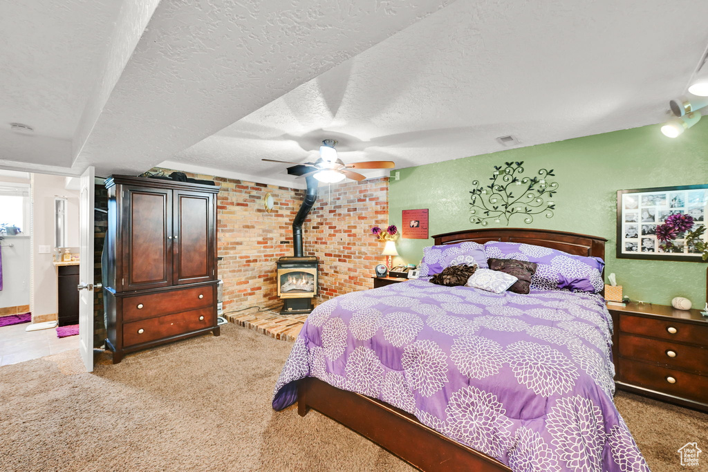 Bedroom featuring a wood stove, light carpet, a textured ceiling, and ceiling fan