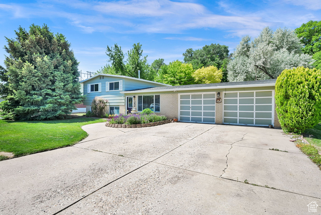 Tri-level home featuring a garage, concrete driveway, brick siding, and a front lawn