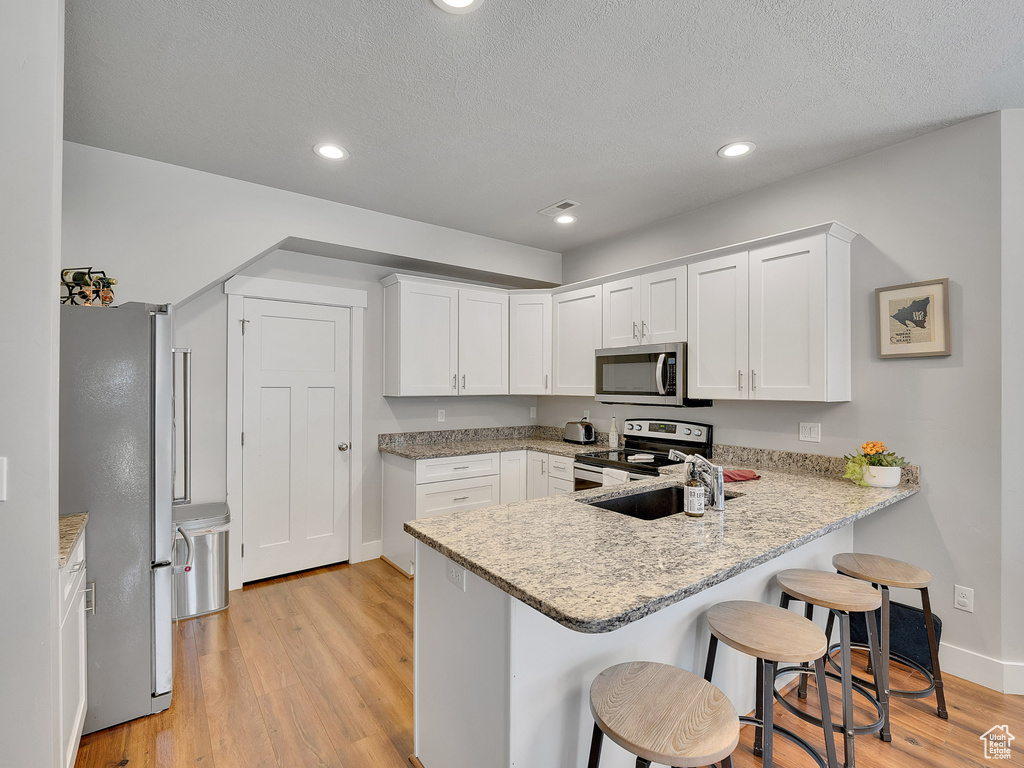 Kitchen featuring appliances with stainless steel finishes, baseboards, a peninsula, a breakfast bar, and light wood-type flooring