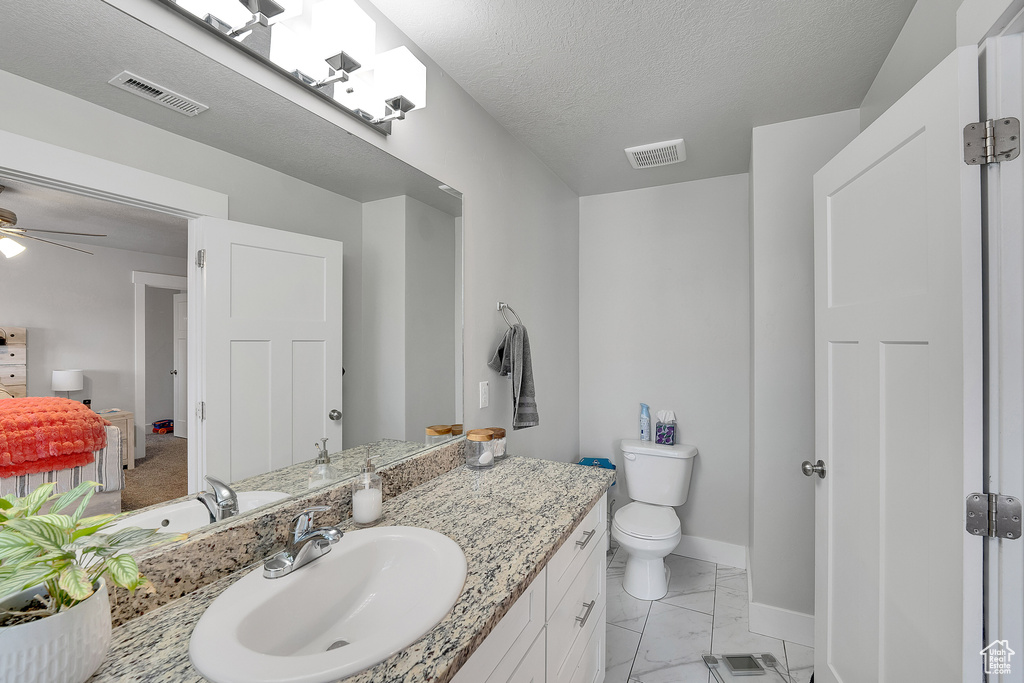 Bathroom featuring baseboards, vanity, toilet, ceiling fan, and marble look tiles