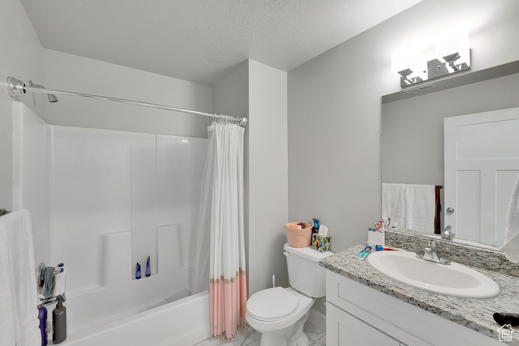 Full bath featuring marble finish flooring, vanity, toilet, shower / bath combination with curtain, and a textured ceiling
