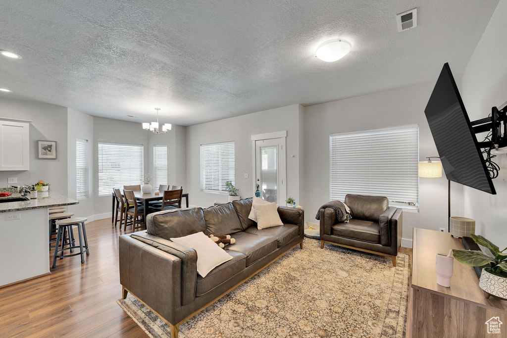 Living area with a chandelier, wood finished floors, a textured ceiling, baseboards, and recessed lighting
