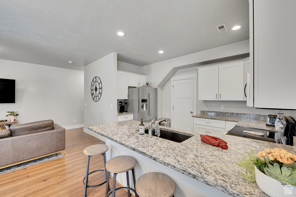 Kitchen featuring black / electric stove, a sink, high end fridge, light wood-style floors, and light stone counters