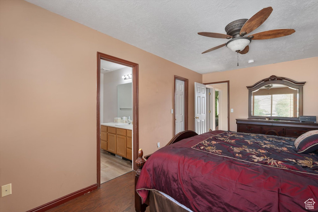 Bedroom with wood finished floors, a sink, a textured ceiling, connected bathroom, and baseboards