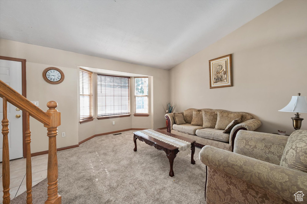 Carpeted living area featuring lofted ceiling, baseboards, and stairs