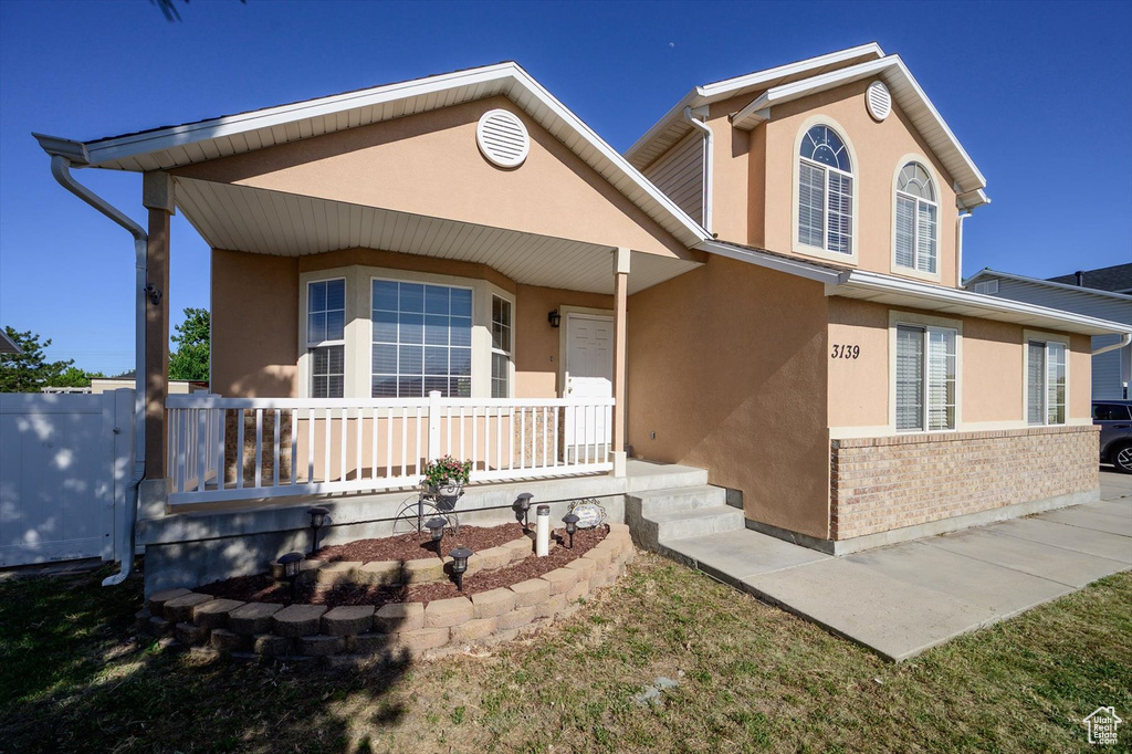 View of front of house with stucco siding, covered porch, and brick siding