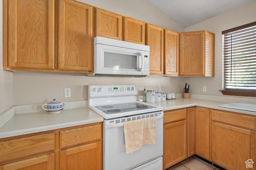 Kitchen featuring white appliances, light countertops, vaulted ceiling, and a sink