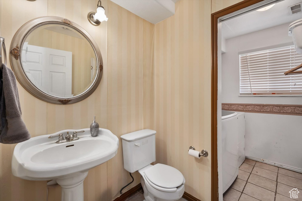Bathroom featuring washer and dryer, wallpapered walls, toilet, tile patterned floors, and a sink