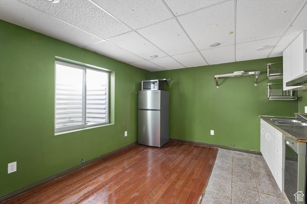Kitchen with freestanding refrigerator, wine cooler, white cabinetry, a sink, and a drop ceiling
