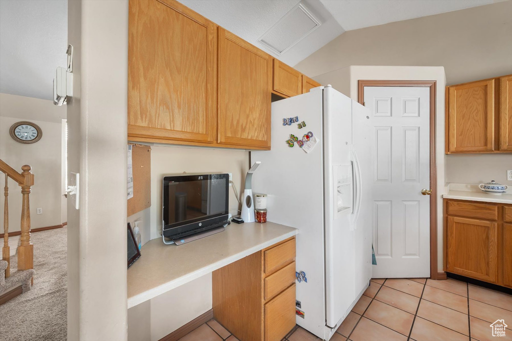 Kitchen featuring white fridge with ice dispenser, light countertops, vaulted ceiling, and light tile patterned flooring