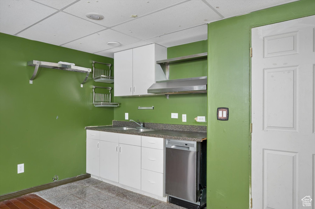 Kitchen with dishwasher, open shelves, dark countertops, a sink, and wall chimney range hood