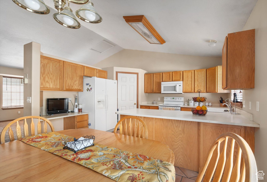 Kitchen with white appliances, a peninsula, healthy amount of natural light, light countertops, and vaulted ceiling