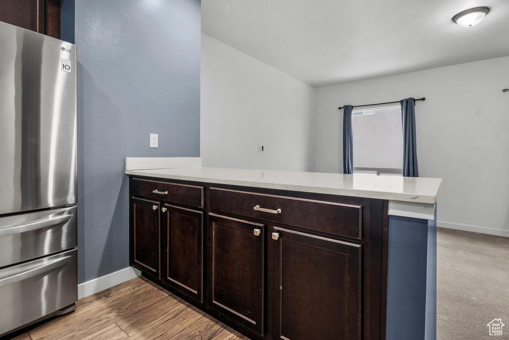 Kitchen featuring freestanding refrigerator, a peninsula, light countertops, and dark brown cabinetry