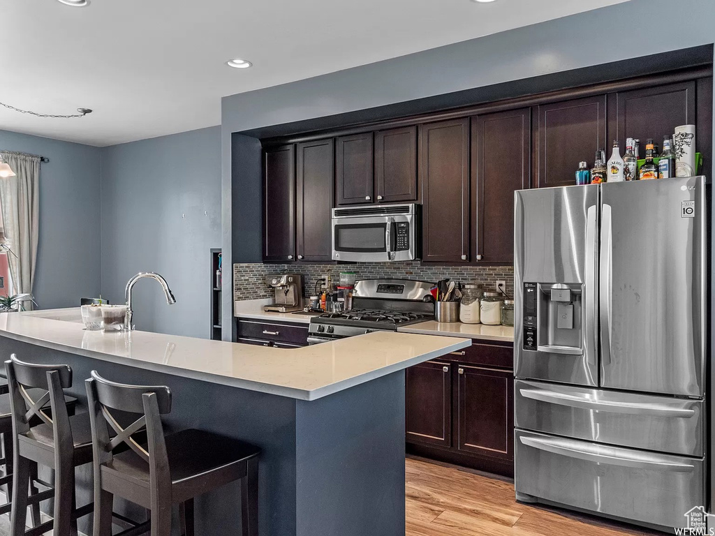 Kitchen with appliances with stainless steel finishes, a kitchen breakfast bar, light countertops, tasteful backsplash, and dark brown cabinetry
