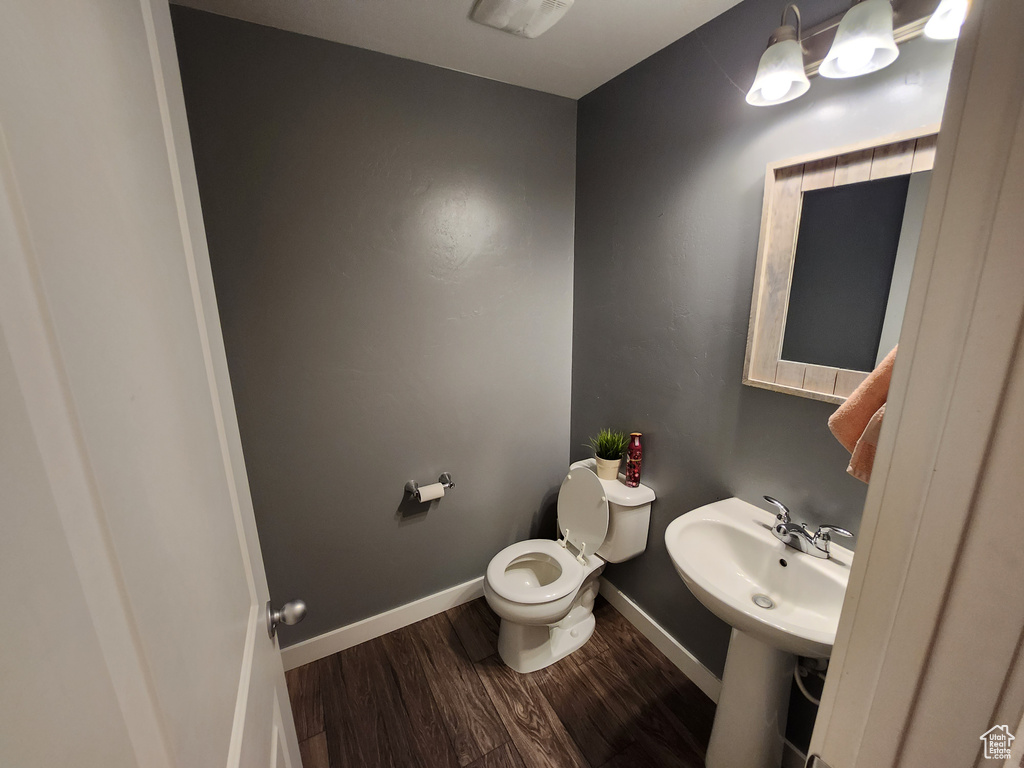 Half bathroom with toilet, wood finished floors, and baseboards