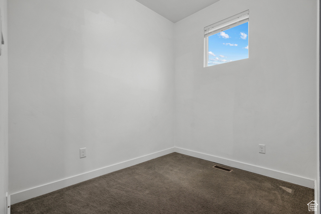 Spare room featuring dark carpet and baseboards