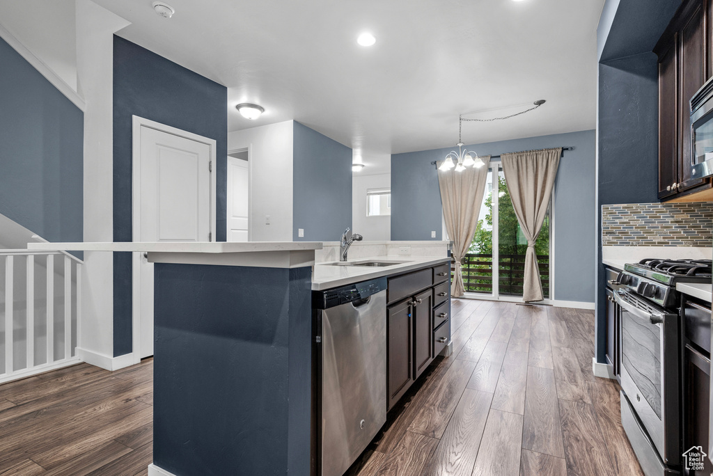 Kitchen with stainless steel appliances, dark wood-type flooring, a chandelier, an island with sink, and backsplash