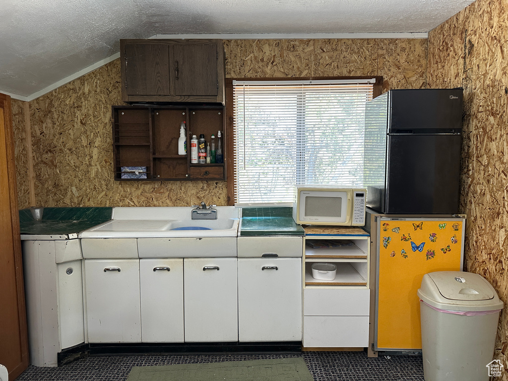 Kitchen featuring white microwave, lofted ceiling, open shelves, white cabinets, and a sink
