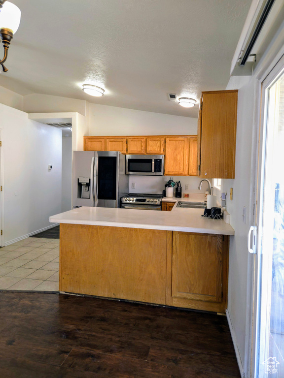 Kitchen featuring appliances with stainless steel finishes, a peninsula, a sink, light countertops, and baseboards