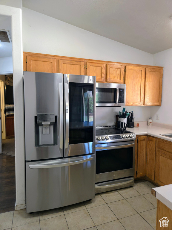 Kitchen featuring appliances with stainless steel finishes, vaulted ceiling, light countertops, light tile patterned floors, and brown cabinetry