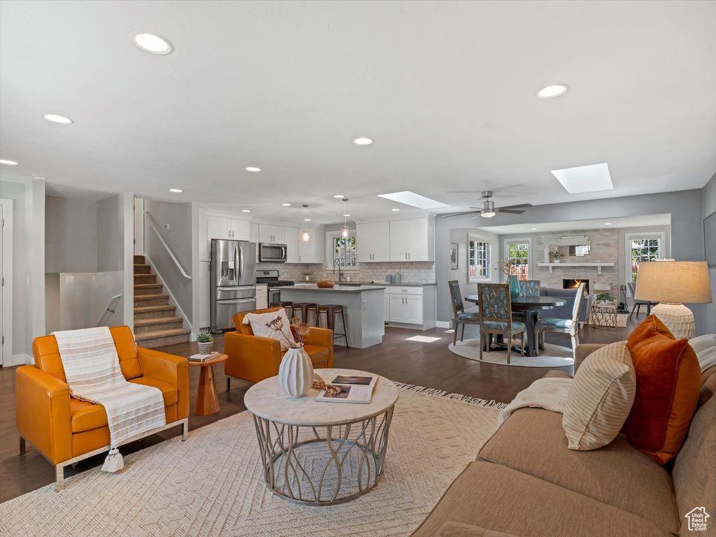 Living room featuring a skylight, dark wood-style flooring, recessed lighting, a ceiling fan, and stairs