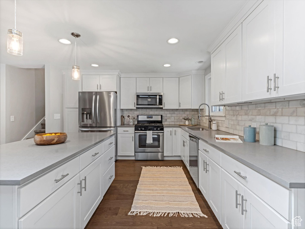 Kitchen featuring appliances with stainless steel finishes, a sink, backsplash, white cabinetry, and decorative light fixtures